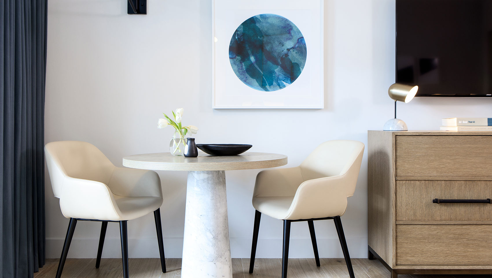 corner seating area with two beige chairs, marble coffee table and abstract blue artwork.