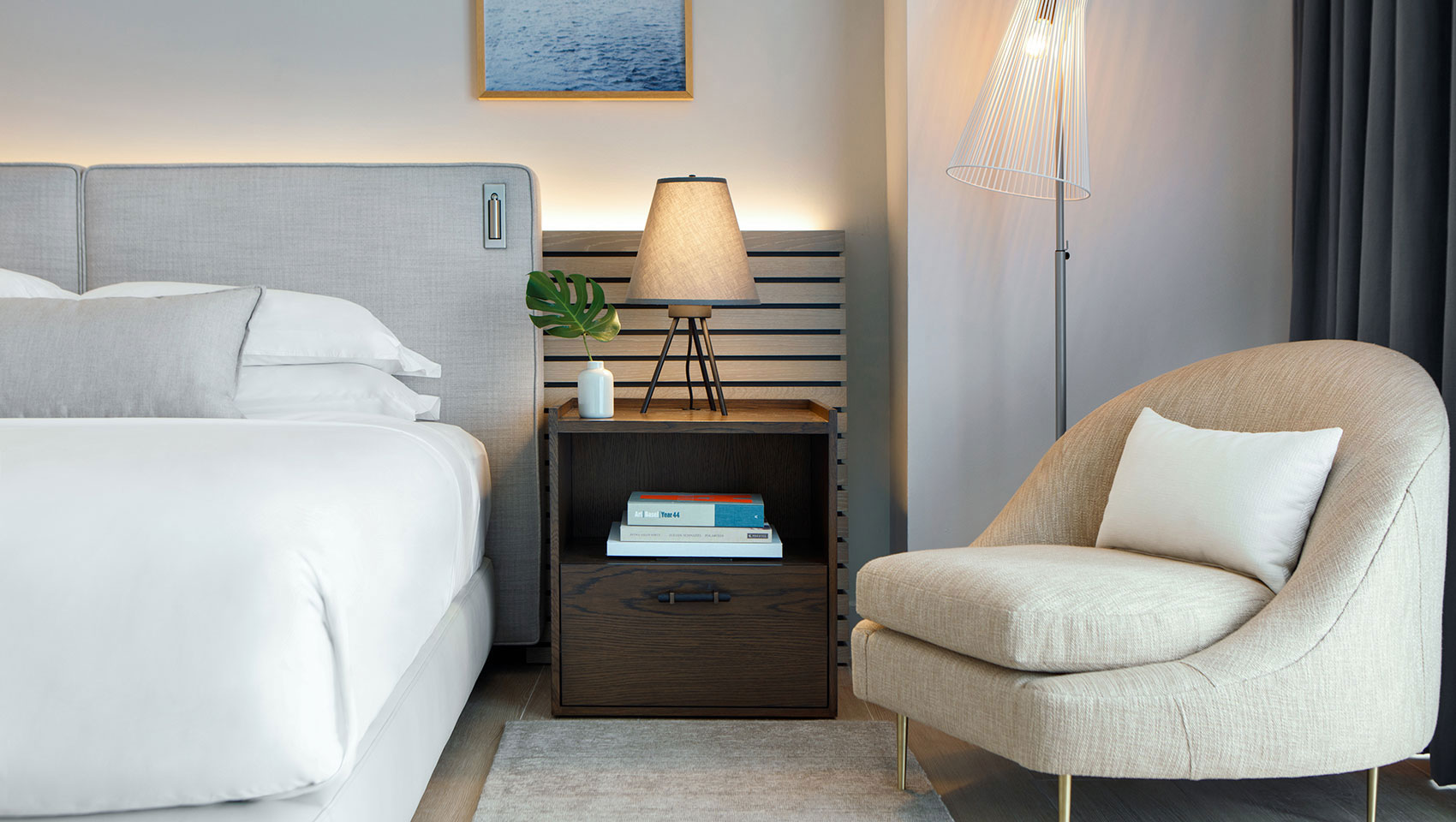 king guestRoom with plush grey headboard, brown nightstand and beige low accent chair.